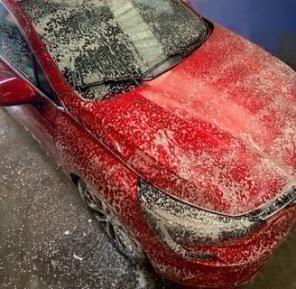 Une voiture rouge recouverte de mousse lors d'un nettoyage