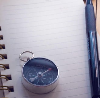 A compass on top of a notebook, with a pen and camera on the side