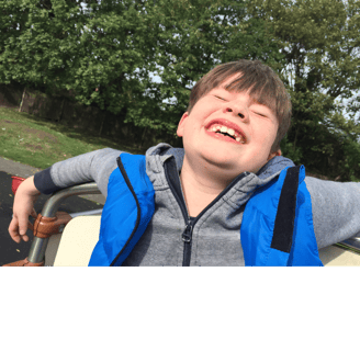 a young boy smiling and laughing while standing in a park. Autista alegre