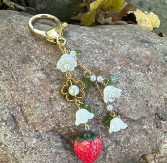 strawberry and flowers key chain with gold tone metal clasp and chain, laying on a rock