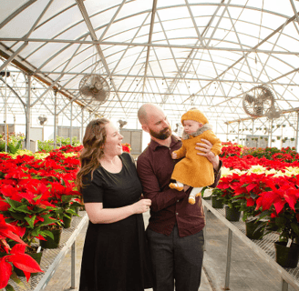 a man and woman holding a baby in a greenhouse