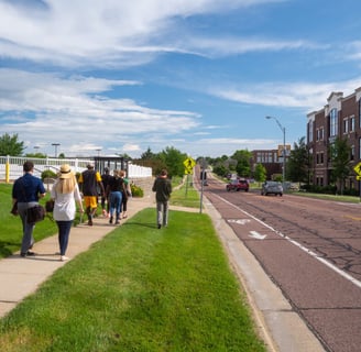 People walking on a sidewalk next to a street with a painted bike lane