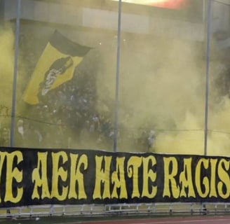 Leidenschaftliche AEK-Athen-Fans in gelb-schwarzen Farben mit Fahnen und Pyrotechnik auf den Rängen des Agia-Sofia-Stadions.