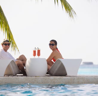 two people sitting on lounge chairs in front of a pool