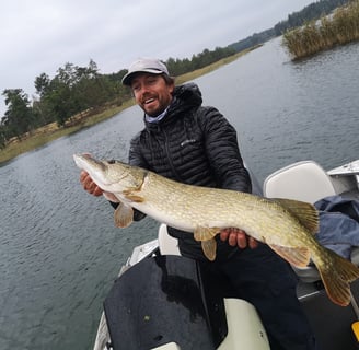 A man is on a boat, he is happy to have caught a big pike in Sweden.