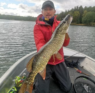 un homme est a genoux dans un bateau de pêche en suède , il tient un beau brochet , il est heureux