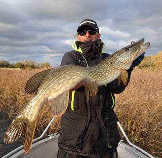 a man is on a fishing boat with fishing escape sweden, he is holding a nice pike in sweden.