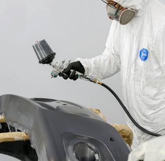 a man in a white suit and a white coat painting a car at fix collision center