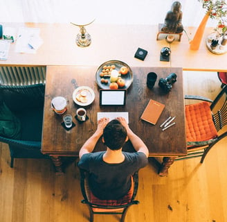 A top-down view of a writer working at a wooden table with a laptop, notebook, coffee, and snacks, surrounded by creative too