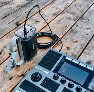 A professional music production setup featuring a Maschine+ controller and connected power source on a wooden table