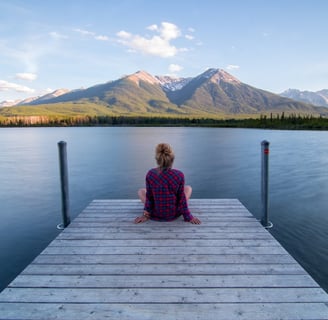 a woman sitting on a dock with mountains in the background