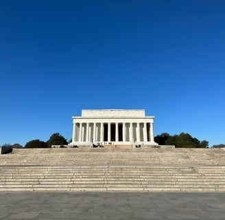 The Lincoln Memorial, a large white building with columns in front of of a blue sky