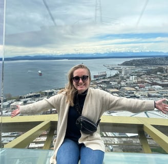 a woman on top of the space needle with the puget sound and olympics in the background