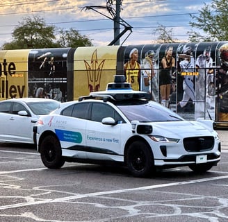 a white car driving down a street with a light rail train behind