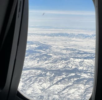 a view of a plane window looking out over a snowy landscape