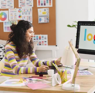 a woman sitting at a desk with a computer monitor and a laptop