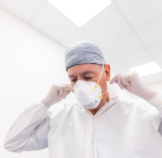 a man in a white lab coat and gloves is putting on a respirator