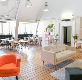 A modern co-working space with worktables, a red chair, and beige sofe