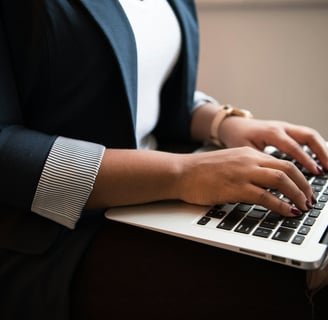 a woman in a white shirt and navy blazer sitting and using a laptop