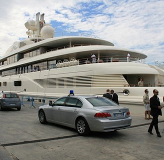 Security vehicle with flashing lights near a 130-meter luxury yacht in Italy, ensuring VIP safety.