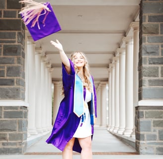 A woman in a purple graduation gown throwing a purple graduation cap