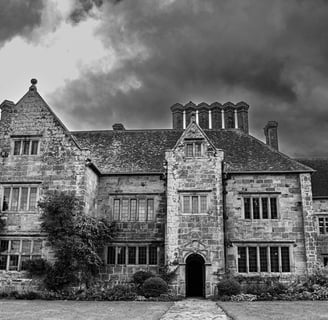 A black & white photos of National Trust Batemans set against stormy looking clouds.