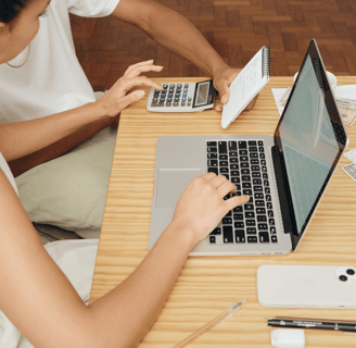 Couple working at a laptop with phone, papers, and calculator on a wooden desk
