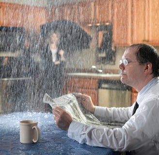 Man overwhelmed by indoor water damage due to a roof leak, highlights the importance of insurance claim assessment