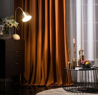 moody room, orange curtains, gold candles with a basked of fruit on black table, neutral curtains