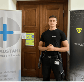 Eine Sicherheitskraft in "SECURITY"- Shirt vor einer Tür