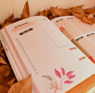 Planner hebdomadaire ouvert sur une page to-do, posé sur un lit de feuilles mortes
