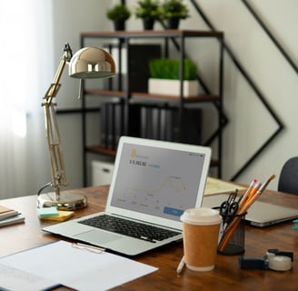 a laptop computer sitting on a desk with a lamp, pencil cup, paperwok, and a cup of coffee