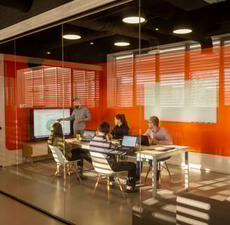 Wide shot through glass walls of a presentation during a ptojrvt team meeting of five people