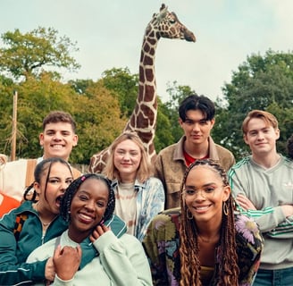 The Heartstopper ensemble cast posing in front of giraffe during season 3 filming.