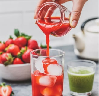 Pouring strawberry puree over ice in a tall glass.