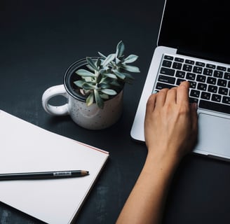Mesa com bloco de anotações e pessoa digitando em notebook