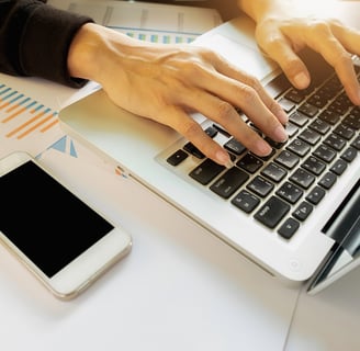 Mulher digitando em um notebook com um celular ao lado