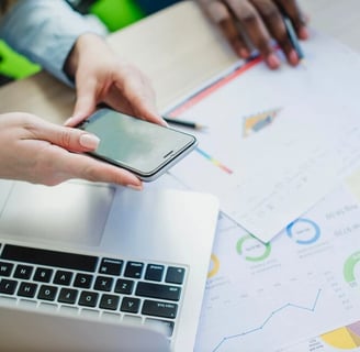 Duas pessoas mexendo em papéis, notebook e celular na mesa