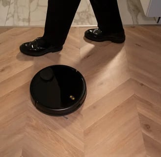 a person standing on a wooden floor with a robot vacuum