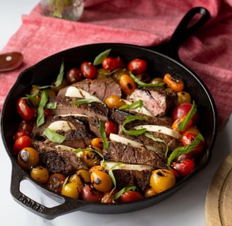 a cast iron skillet with steak steak and tomatoes
