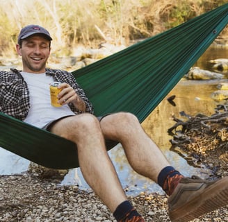 a man sitting in a hammock with a beer