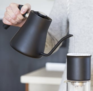 a person pouring water into a cup of coffee