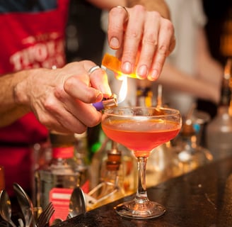 Ein Mixologe erhitzt eine Orangenscheibe mit einem Feuerzeug über einem Cocktail.