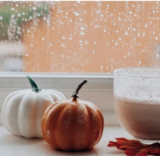 Cozy living: A window sill with pumpkin latte, candlelight, autumn decor, and raindrops on glass.