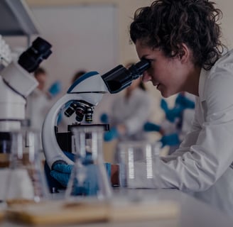 a woman in a lab coat is looking through a microscope