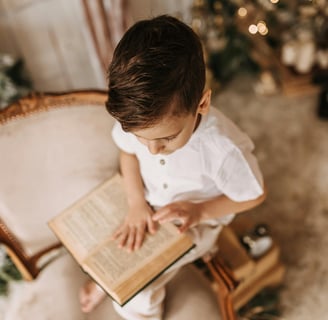 a young boy is sitting in a chair and reading a book