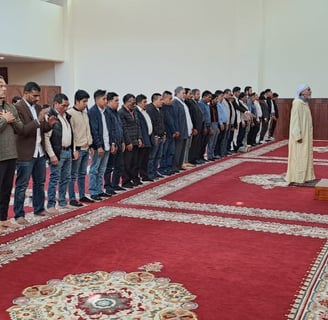 a group of men standing in line performing salat at Imam Malik Mosque