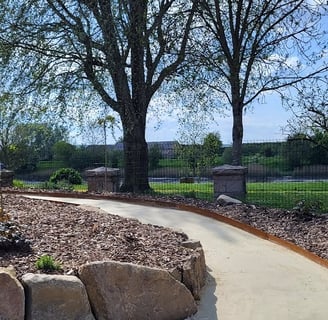 Allée dallée en béton décoratif dans un jardin paysager avec arbres et massifs végétalisés