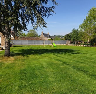 Pelouse parfaitement tondue dans un jardin paysager ensoleillé avec une maison en arrière-plan