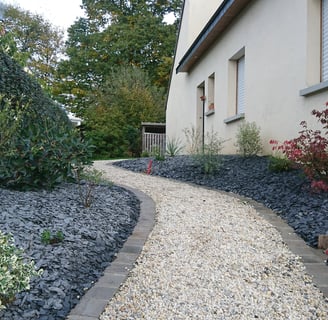 Allée en gravier clair bordée de pas japonais et de massifs paysagers le long d'une maison